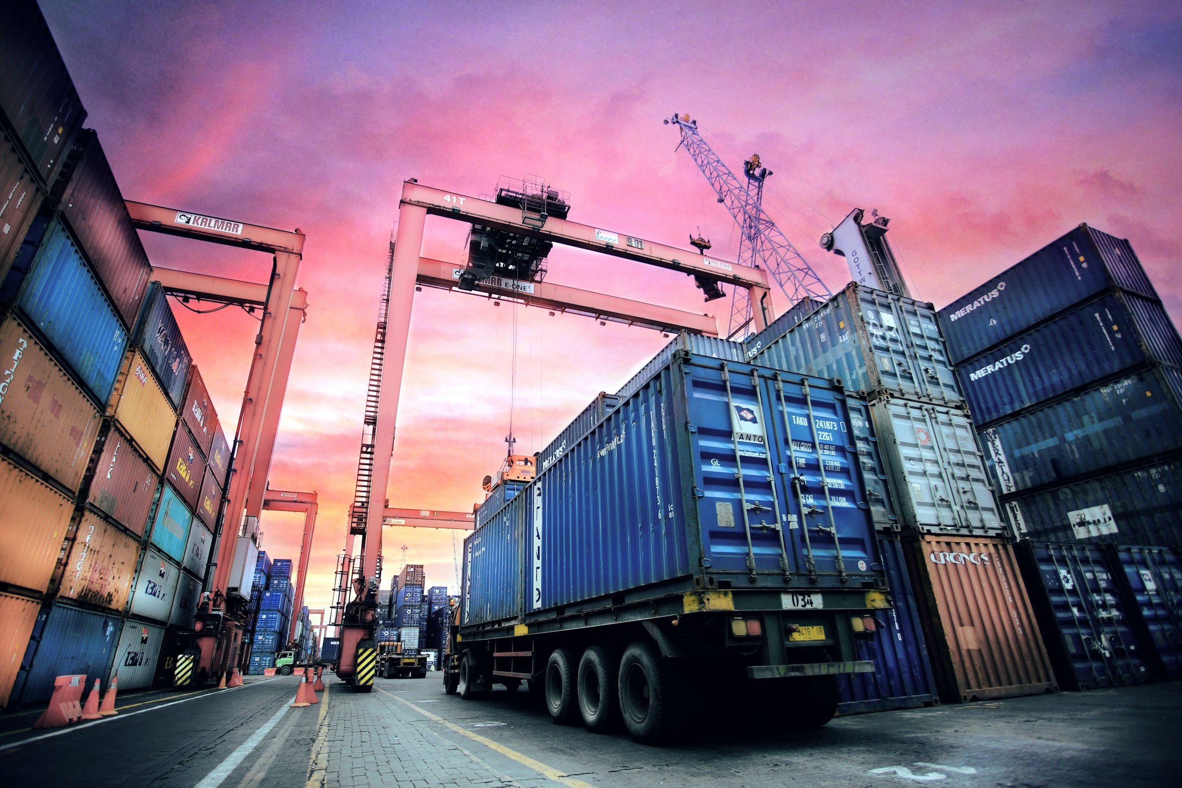 Truck carrying a shipping container through a container yard at dusk